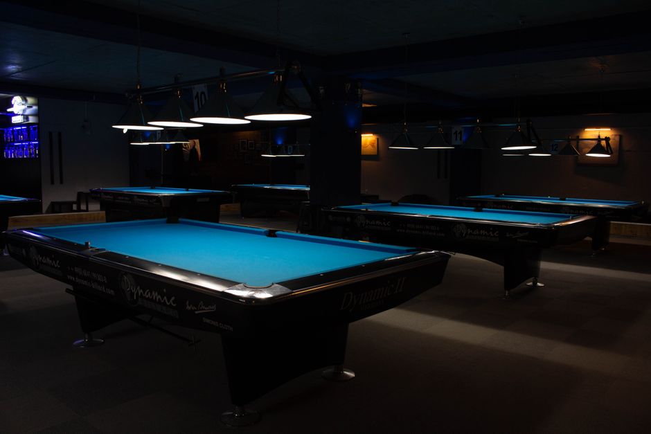 A row of empty billiard tables in a dim room